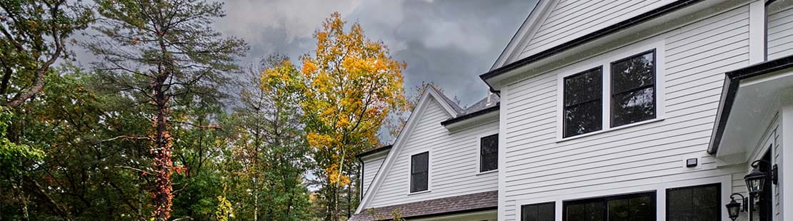 Trees and home surrounded by dark stormy sky.