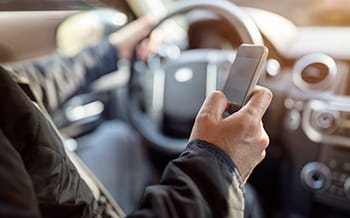 Person with one hand on a steering wheel and the other holding a cell phone