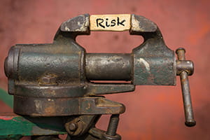 vise holding a piece of wood with the word "risk" written on it