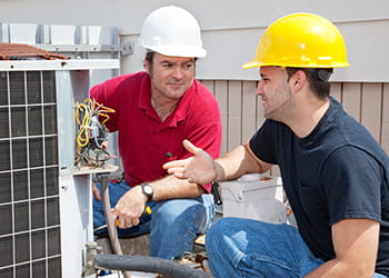 Two men in hard hats looking at an air conditioning unit