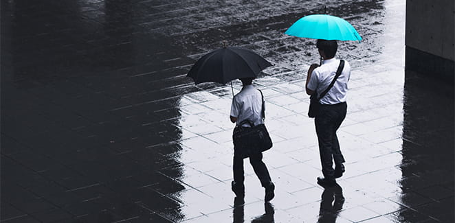 Two people in suits walking in the rain holding umbrellas