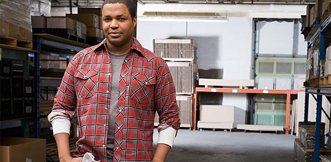 African-American man in a red plaid shirt standing in a warehouse.